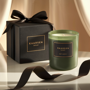  Luxe groene geurkaars in een elegante glazen houder met een zwarte en gouden label, gepresenteerd naast een stijlvolle zwarte geschenkdoos met een gouden logo en een zwarte satijnen strik, van Kaarsen Outlet.